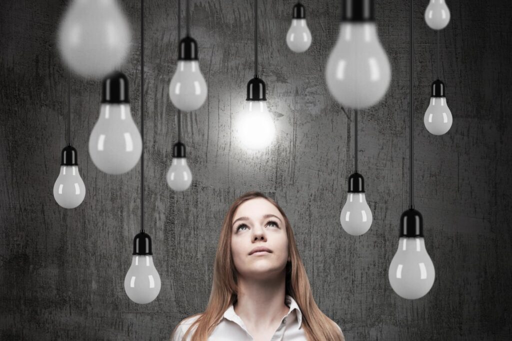 A woman, business owner, looking up at several lightbulbs, one illuminated, symbolizing insight and solutions for managing GST/HST debt through proposals or bankruptcy for Canadian businesses.